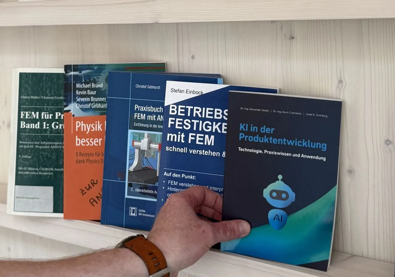 The printed book KI in der Produktentwicklung being taken off a shelf, shelved beside Betriebsfestigkeit mit FEM, Praxisbuch FEM mit ANSYS and FEM fuer Praktiker.