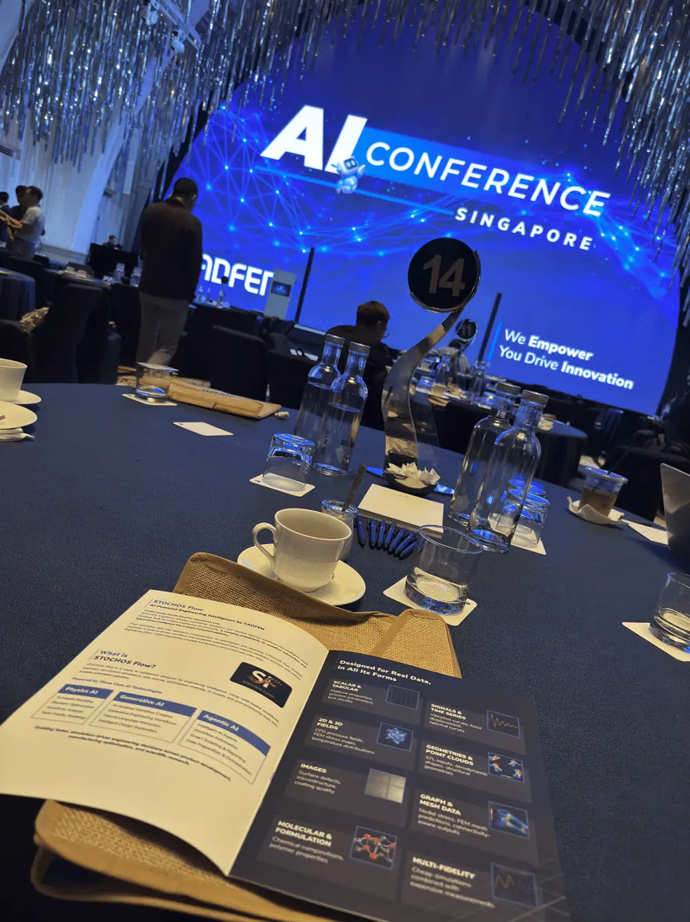 Conference table with a STOCHOS Flow brochure in the foreground and the AI Conference Singapore stage behind it