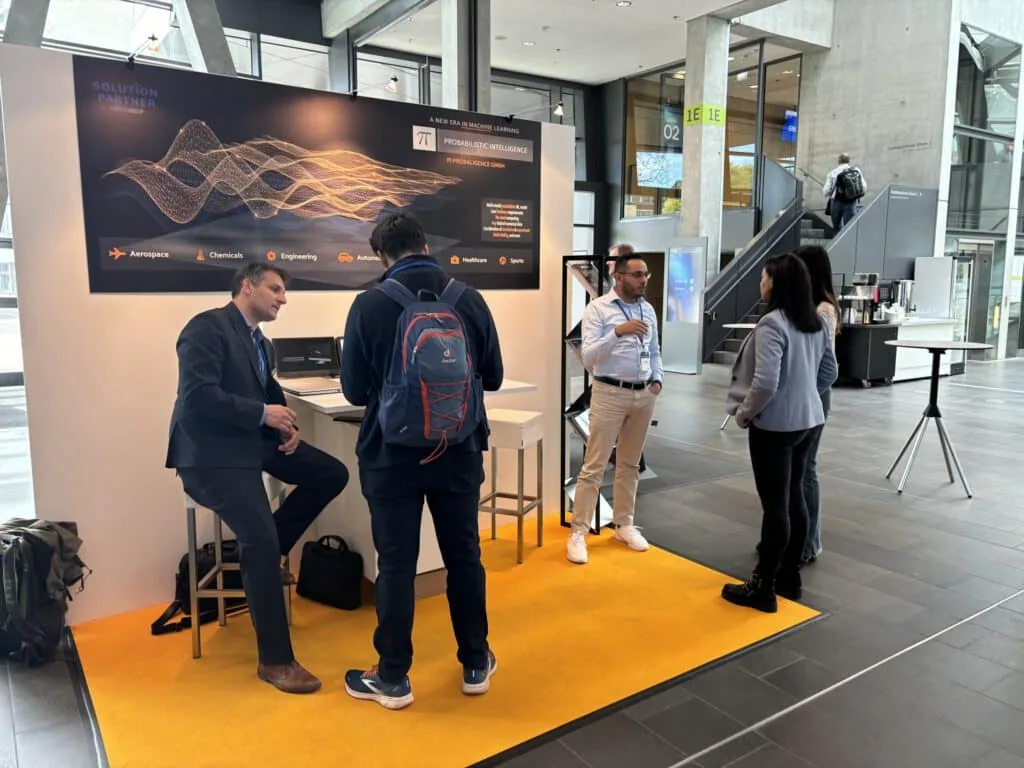 The PI Probaligence booth at the CADFEM Conference 2024, with team members talking to visitors in front of a dark Probabilistic Intelligence banner listing aerospace, chemicals, engineering, automotive, healthcare, and sports.