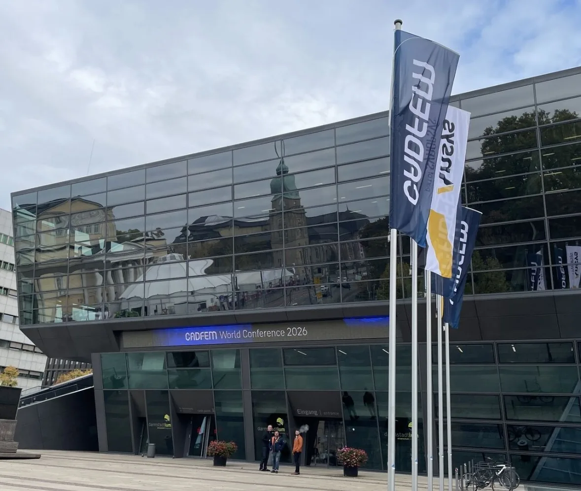 Glass facade of the darmstadtium congress center with the sign CADFEM World Conference 2026 above the entrance and CADFEM and Ansys flags in front.