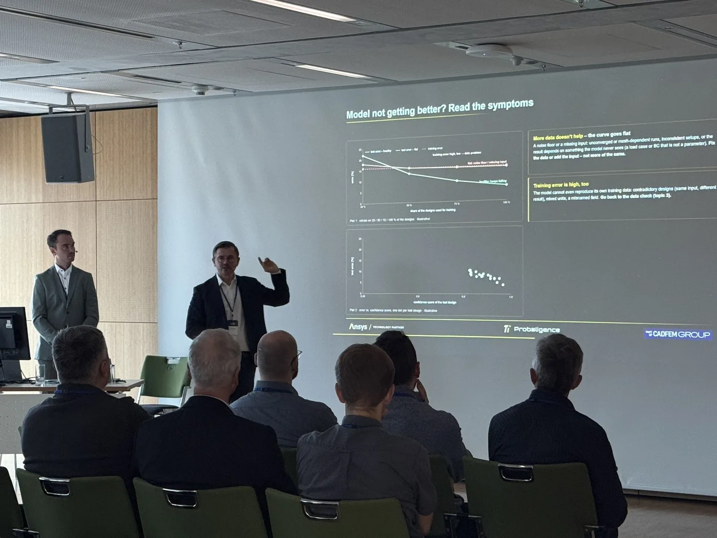 Two presenters in front of a slide titled Model not getting better? Read the symptoms, with two diagnostic plots, seen from the back of the audience.