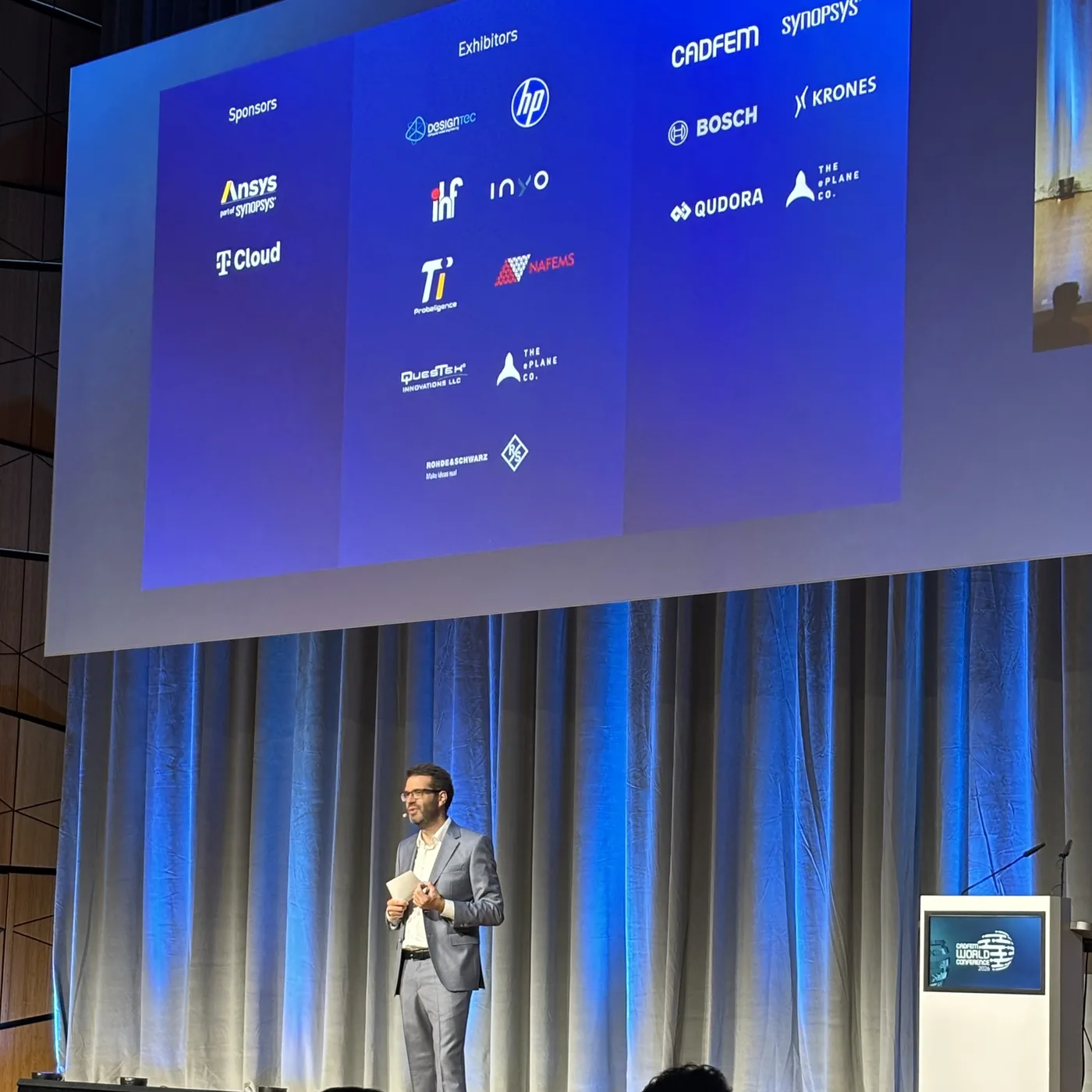 The opening plenary: a speaker under a slide listing the sponsors, exhibitors and keynote companies of the conference, with the PI Probaligence logo among the exhibitors.