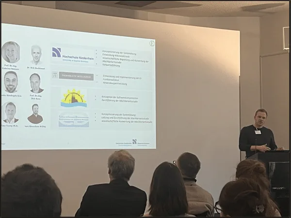 Speaker presenting the KIP project consortium slide, with partner logos and team portraits, to a seated audience