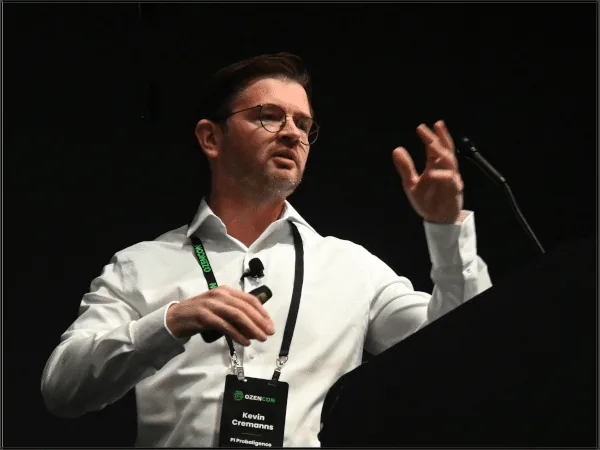 Dr. Cremanns speaking at a podium at OzenCon 2025, gesturing mid-presentation and wearing an OzenCon badge