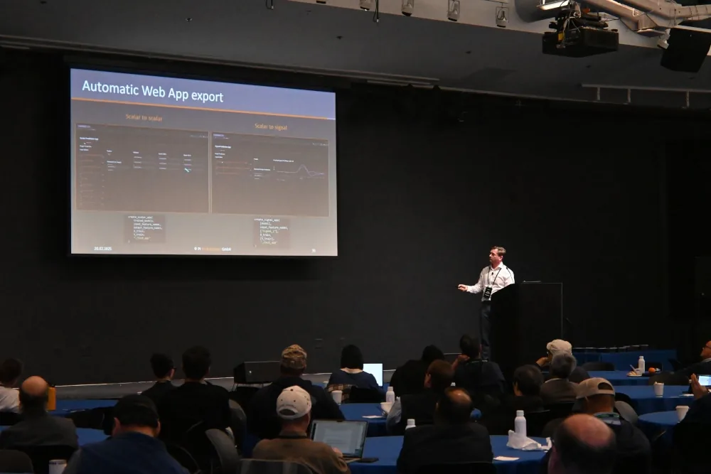 Conference audience watching a STOCHOS presentation slide titled Automatic Web App export at OzenCon 2025