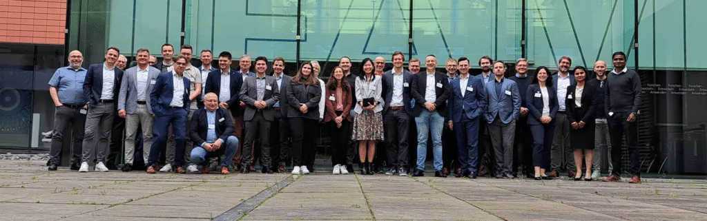 Group photo of the participants of the 2nd Smart Paint Factory Alliance Workference in front of the glass facade of Fraunhofer IFAM in Bremen.